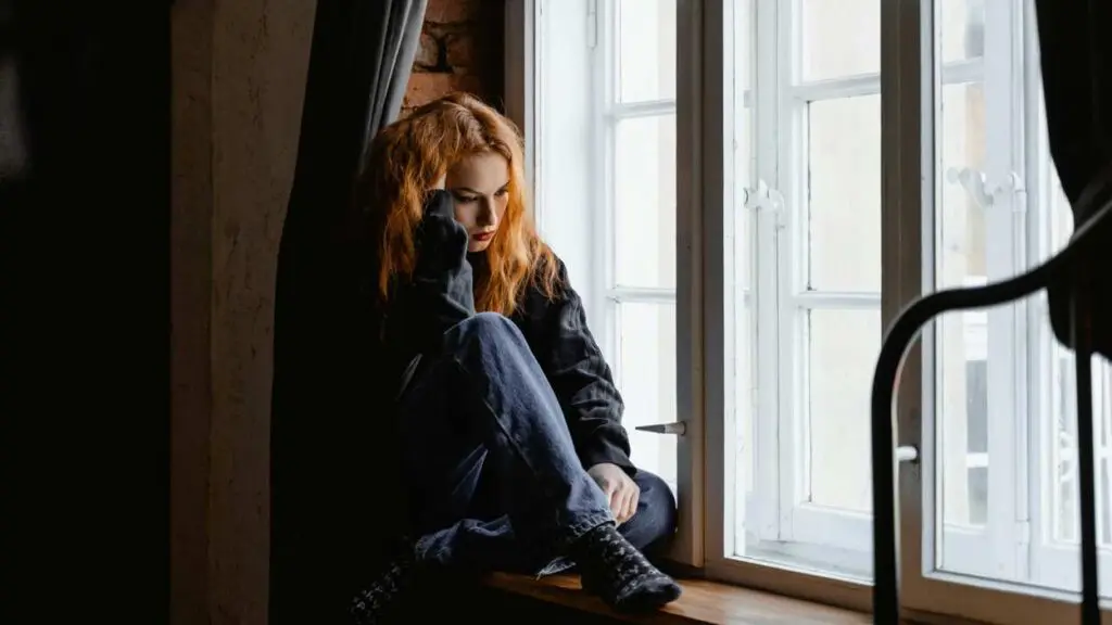 woman sitting in windowsill looking sad representing story on grieving in holidays