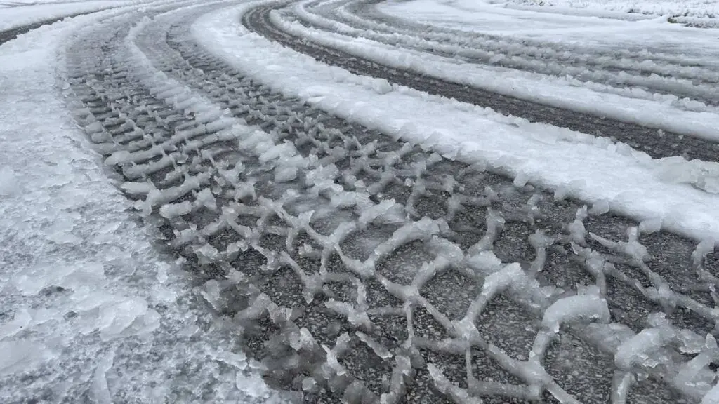 Winter road conditions with a tire track going through snow.