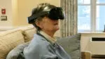 A senior woman in a blue sweater wears a virtual reality headset and looks up