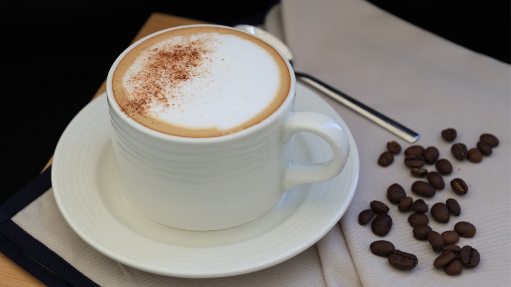 close up of cup of coffee with foam on top and coffee beans to the side