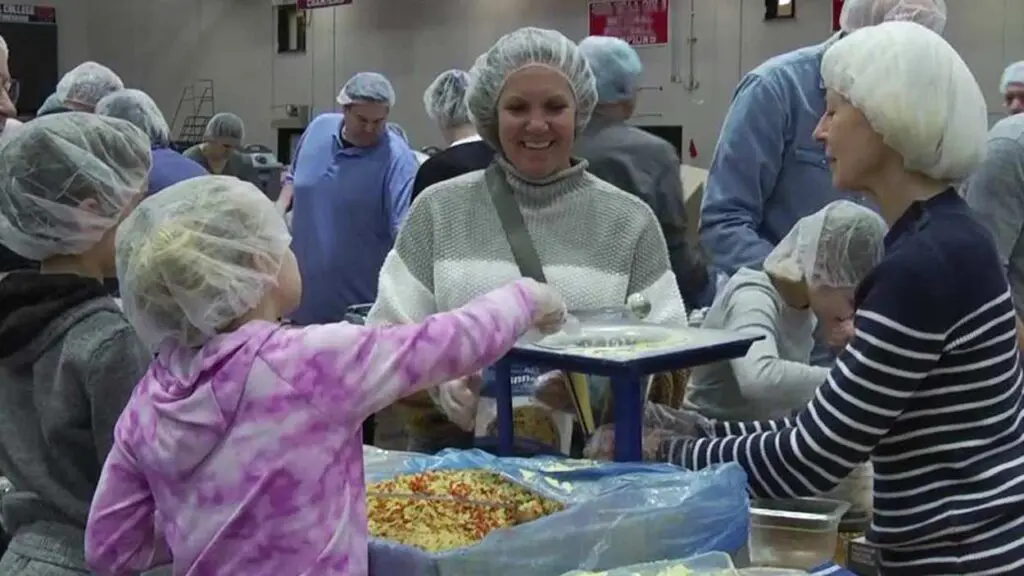 volunteers with hair nets filling meal packs at Feed the Need mobile pack event