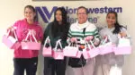 4 people hold pink gift backs in front of a sign that reads Northwestern Medicine.