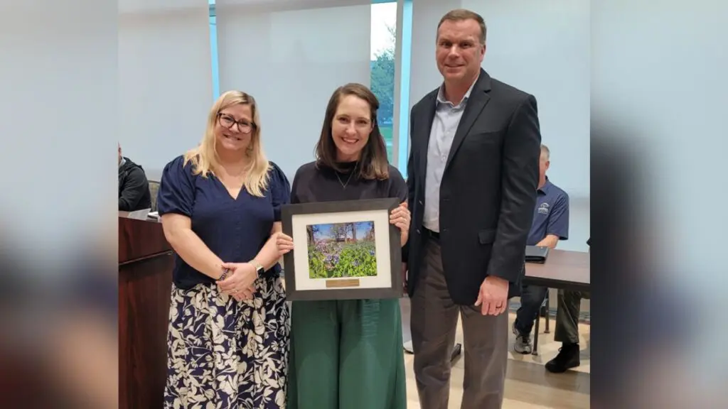 Naperville Park Board Vice President Leslie Ruffing, President Mary Gibson and Executive Director Brad Wilson standing as Gibson holds a plaque with a photo of Knoch Knolls Park