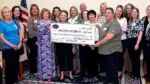 A group of woman stand with a large check made out to "NWC Philanthropy" for $26,124.