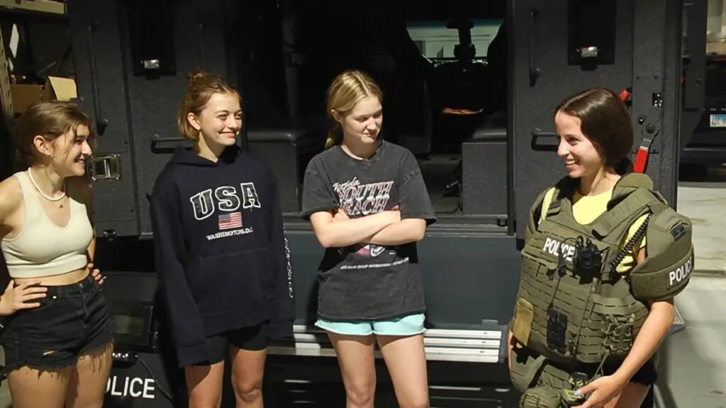 Four teens standing in font of Naperville police vehicle with one in Naperville police garb for summer Youth Academy program