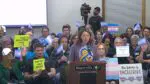 Community members at Naperville School District 203 board meeting weighing in on transgender athlete controversy with both pro and con signs on the issue in background