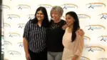 A KidsMatter Teen Philanthropy Initiative mentor hugs two students for a picture at the TPI graduation in front of a KidsMatter backdrop.