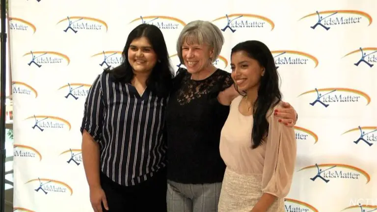 A KidsMatter Teen Philanthropy Initiative mentor hugs two students for a picture at the TPI graduation in front of a KidsMatter backdrop.
