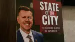 sign of naperville mayor Scott Wehrli with "state of the city: the building blocks of Naperville" over his shoulder