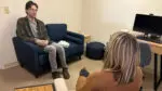 A man sits on a sofa and talks to a woman.