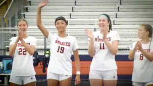 Naperville North girls soccer players smile and wave for lineup introductions against Benet Academy.