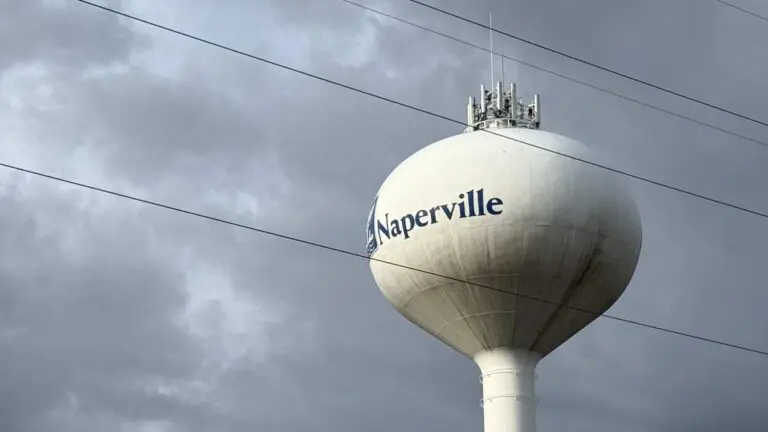 Cell phone tower components atop Naperville water tower with power lines in foreground