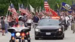 Motorcyclist, car, and a lineup of flags with marchers at the Memorial Day Parade in Naperville