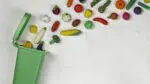 Various pieces of produce flying into a green recycling bin