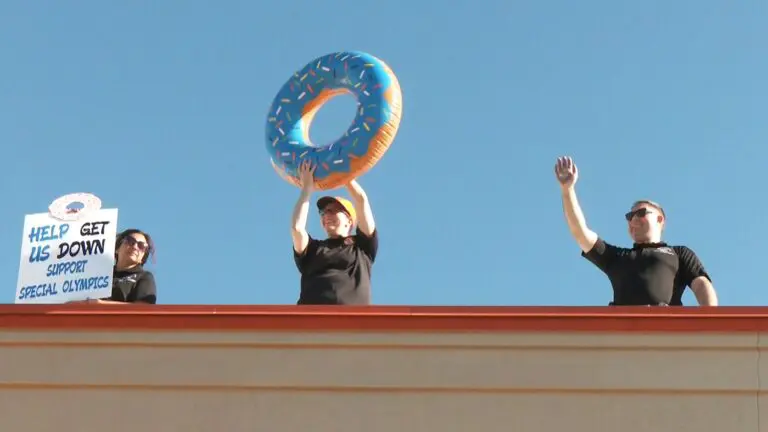 3 police personnel atop a Dunkin' rooftop, one holding a sign, another holding an inflatable donut