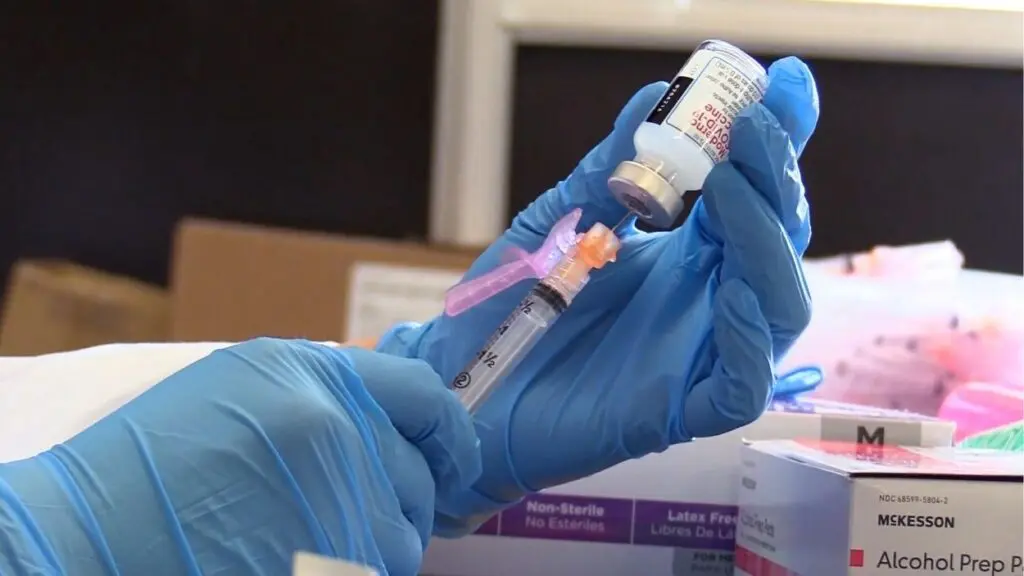 A nurse has a syringe inside a Moderna COVID-19 vaccine bottle, preparing to vaccinate a patient.