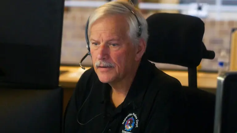Telecommunicator Mike Rafferty seen sitting at his station with phone call headset on, ready to field an incoming emergency phone call