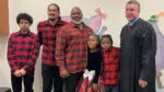 A family in matching red plaid stands next to a smiling judge.