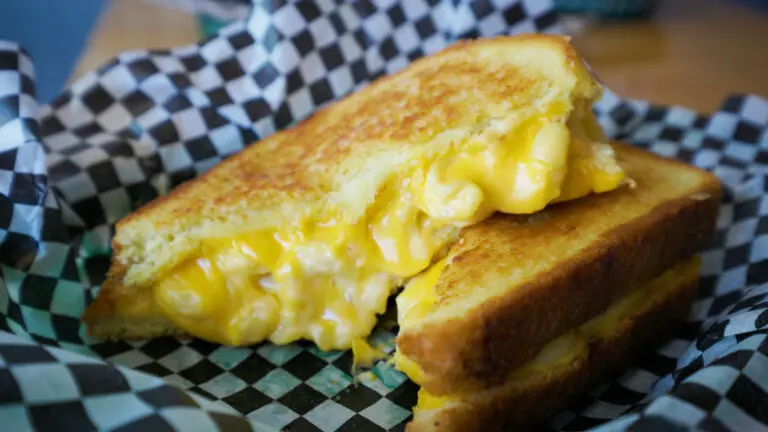 A grilled cheese, filled with mac and cheese, sits sliced open on blue and white checkered parchment paper.
