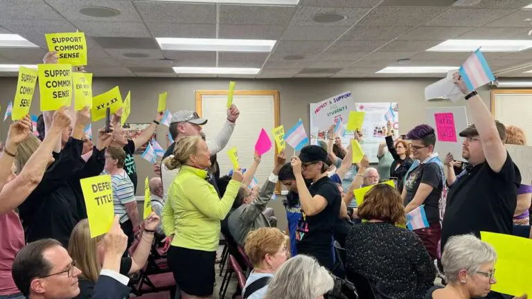A mix of community members holding signs and flags in favor or against transgender athletes participating in teams that align with their gender identity