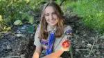 A girl in her scouting uniform in the woods.