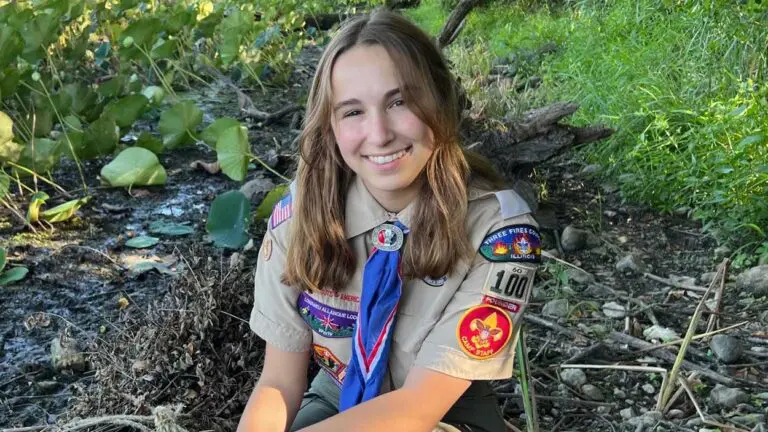 A girl in her scouting uniform in the woods.