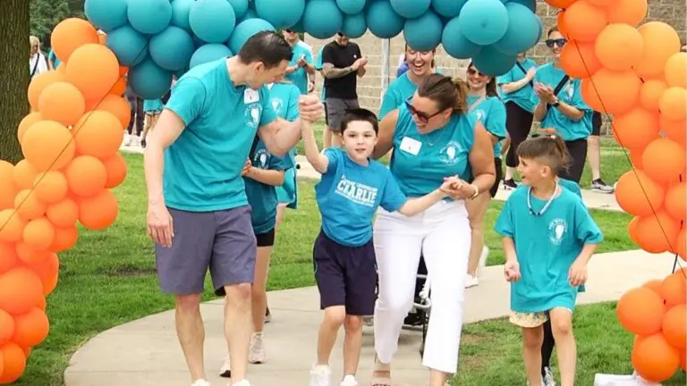Charlie Sims walks with others under a balloon arch at the Team Charlie Walk for Charlie event to combat rare diseases