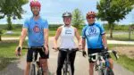Zac Larson, creator of the Solstice Century bike ride stands over his bike alongside two participants Ganerdene Gantumer and Katie Peseski