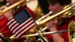 An American flag is in focus, with a trombone player behind it, out of focus.