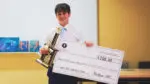 A male high school student stands with a trophy and a giant check for $250 after the BizBuzz "Fish Tank" event.