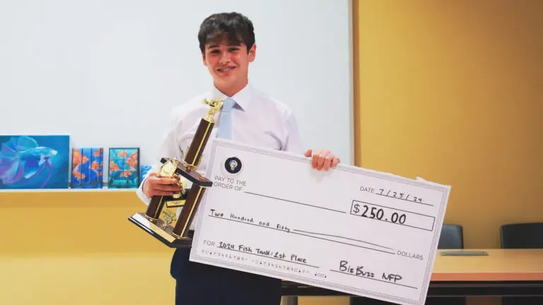 A male high school student stands with a trophy and a giant check for $250 after the BizBuzz "Fish Tank" event.