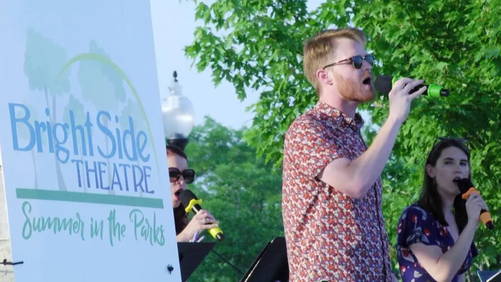 A man singing next to a BrightSide Theatre Summer in the Parks sign