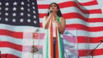 A young woman sings on stage wearing the colors of the Indian flag, with the American flag projected behind her.