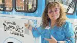 Annette Wehrli stands in front of a trolley and points to the "Naperville Trolley Tours" logo on the side.