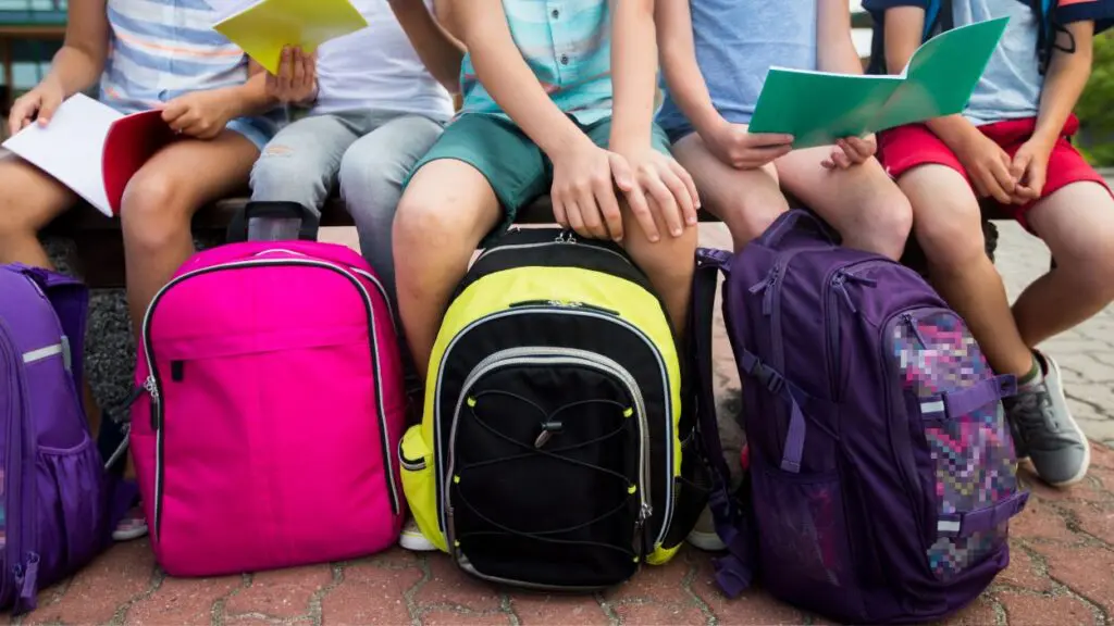 Students seated on bench with backpacks sitting on ground in front of them
