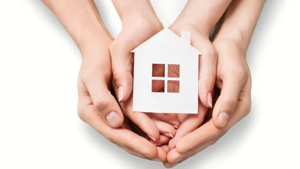 several hands together holding a small wooden home cut-out