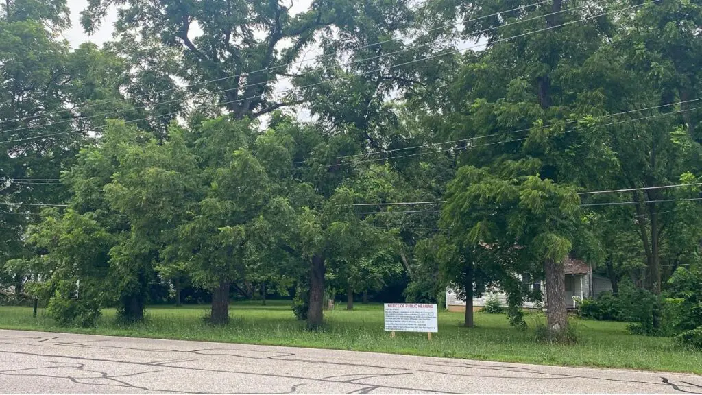 Wide shot of site off of Book Road near Clow Creek Greenway where new subdivision is being proposed - planning and zoning sign and trees in view next to roadway