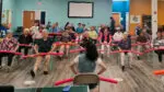 A group of Asian seniors participate in an exercise class with red pool noodles.