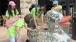 A group of Community Access Naperville participants wear their signature lime green shirts and touch a large, disco ball covered duck statue in Downtown Naperville.