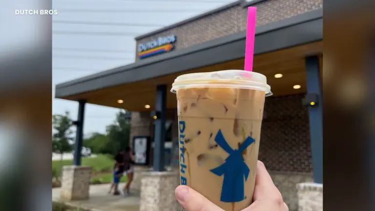 Iced Dutch Bros coffee drink in cup held up in front of Dutch Bros coffee shop