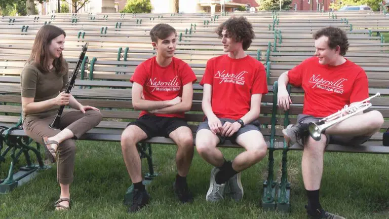 Sydney Phelps, Nick Cristao, Theo Christopherson, and Dayton Melaniphy of the Naperville Municipal Band sit on a bench in Central Park in Naperville.