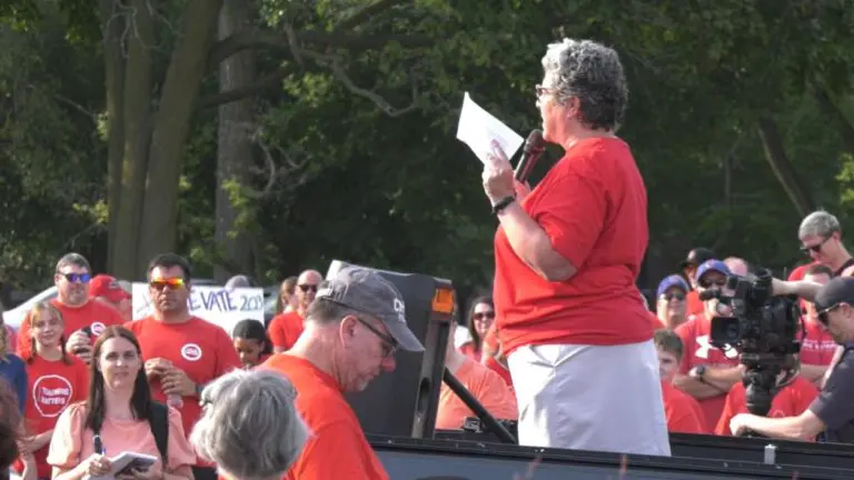 Woman in red shirt with microphone speaking to crowd ini red shirts at rally