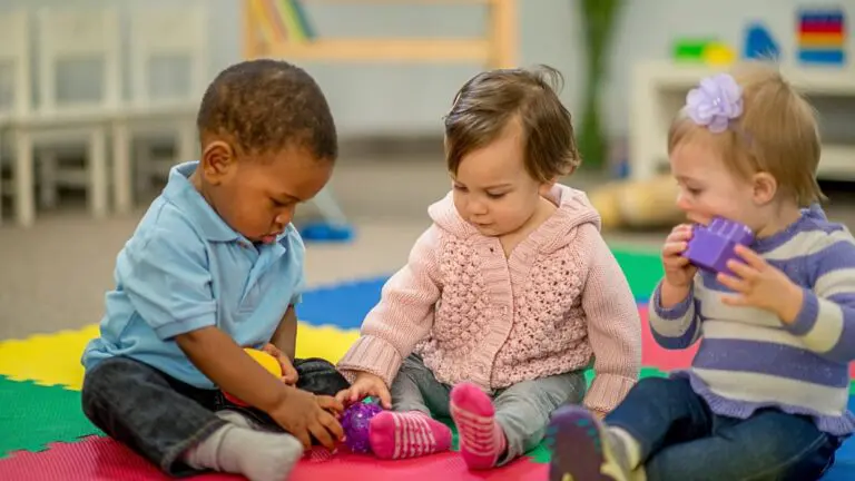 Three toddlers sitting on a mat playing with toys
