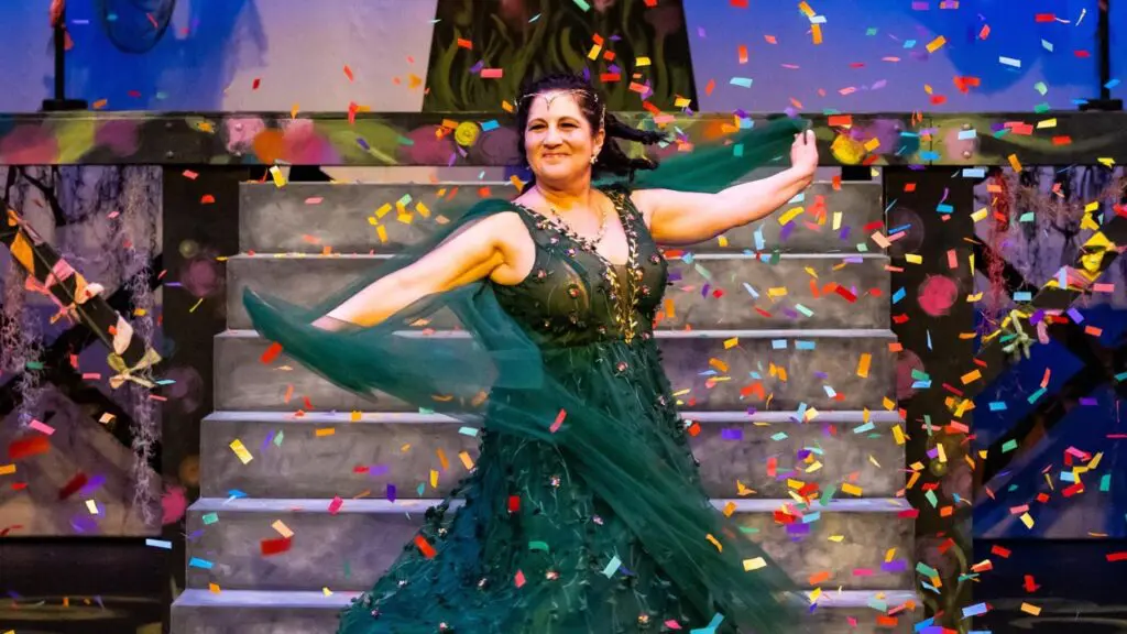 A woman in a green dress twirls on a stage as multicolored confetti falls.