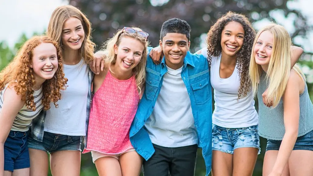 Group of teens standing with arms around each other smiling at camera