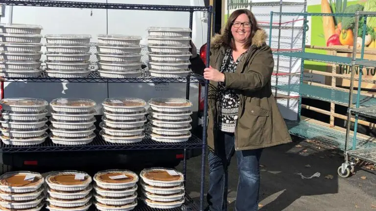 A woman stands with a three-tiered cart full of donated pumpkin pies.