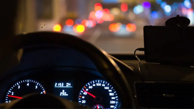 Dashboard of car looking out through windshield at traffic at night