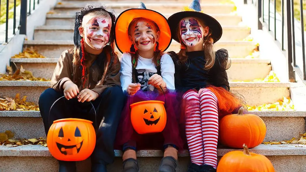 three kids dressed up in Halloween costumes sitting on front porch steps with trick or treat baskets