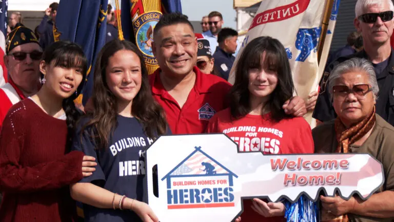 Staff Sergeant Tomee Phetsisouk with family holding giant cut-out key posing for a photo outside his new home in south Naperville