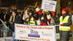 People hold Parade with a Purpose Holiday Parade of Lights banner